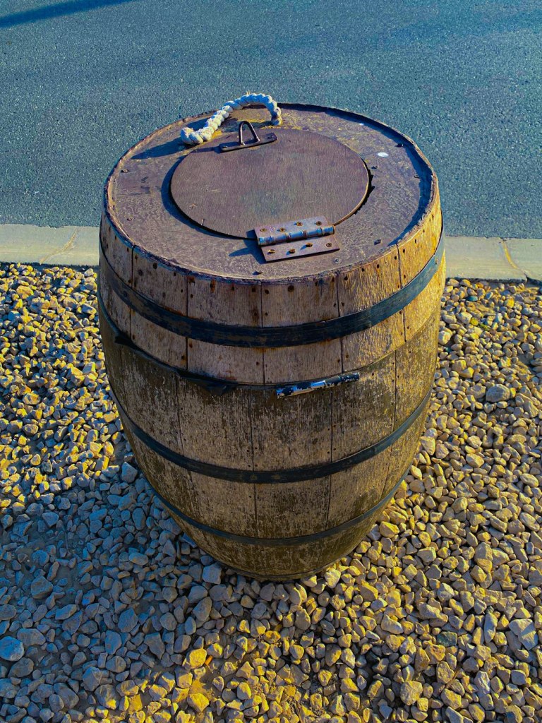 a wooden barrel sitting on top of a gravel road