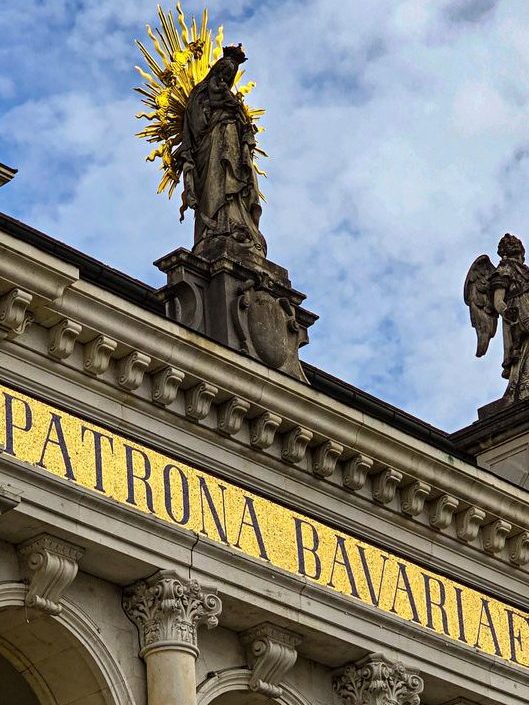 A statue of the Virgin Mary at the top of an arcade with the inscription 'Patrona Bavariae.'